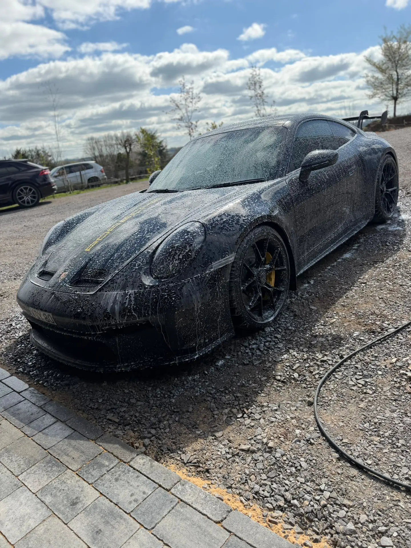 Black Porsche 911 GT3 covered in snow foam during a wash by Pristine
